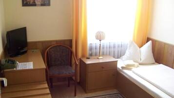A hotel room with a bed, a desk with a lamp, a chair, and a television.