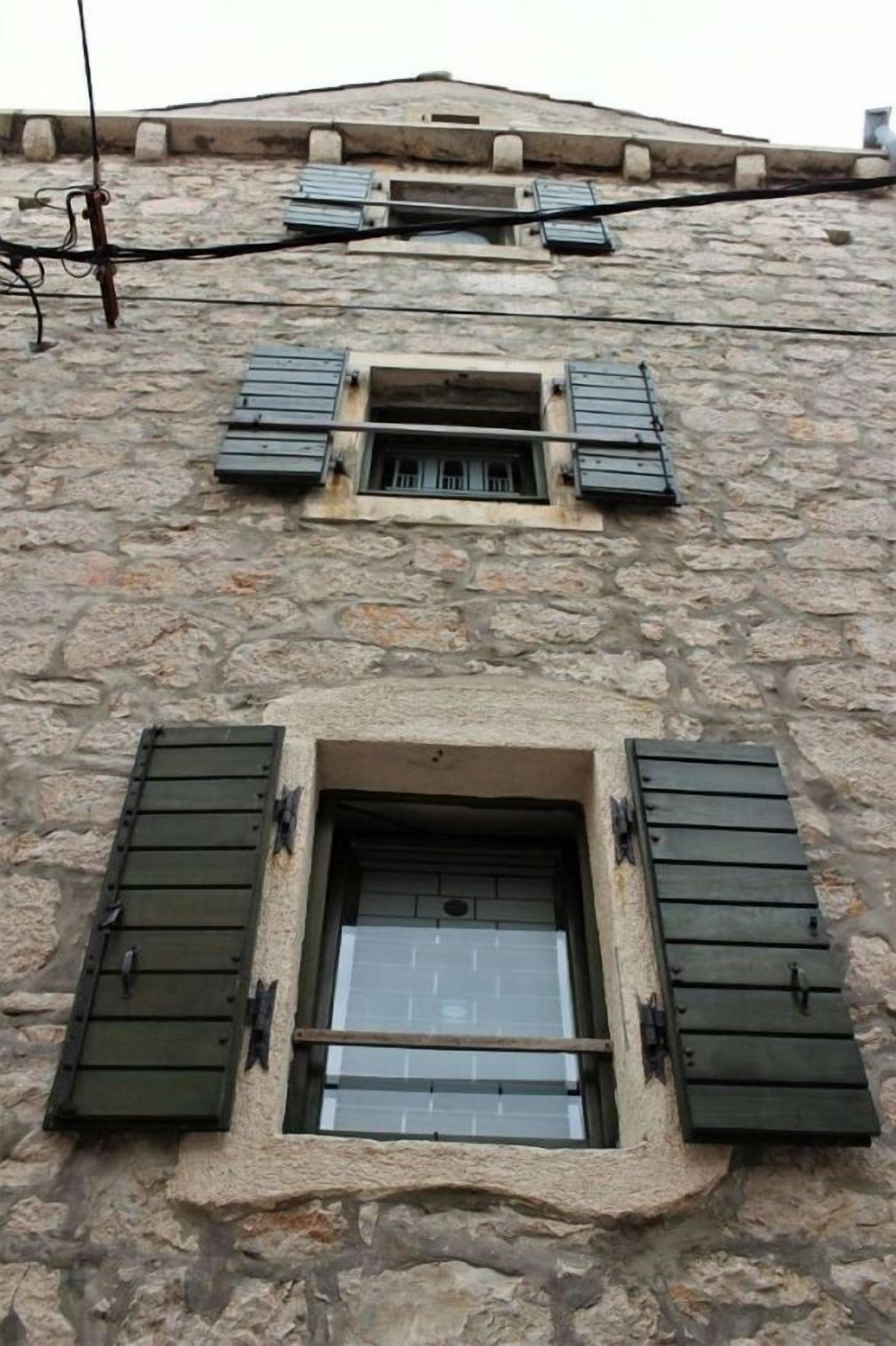 Un edificio in pietra con due finestre, ciascuna con persiane verdi.