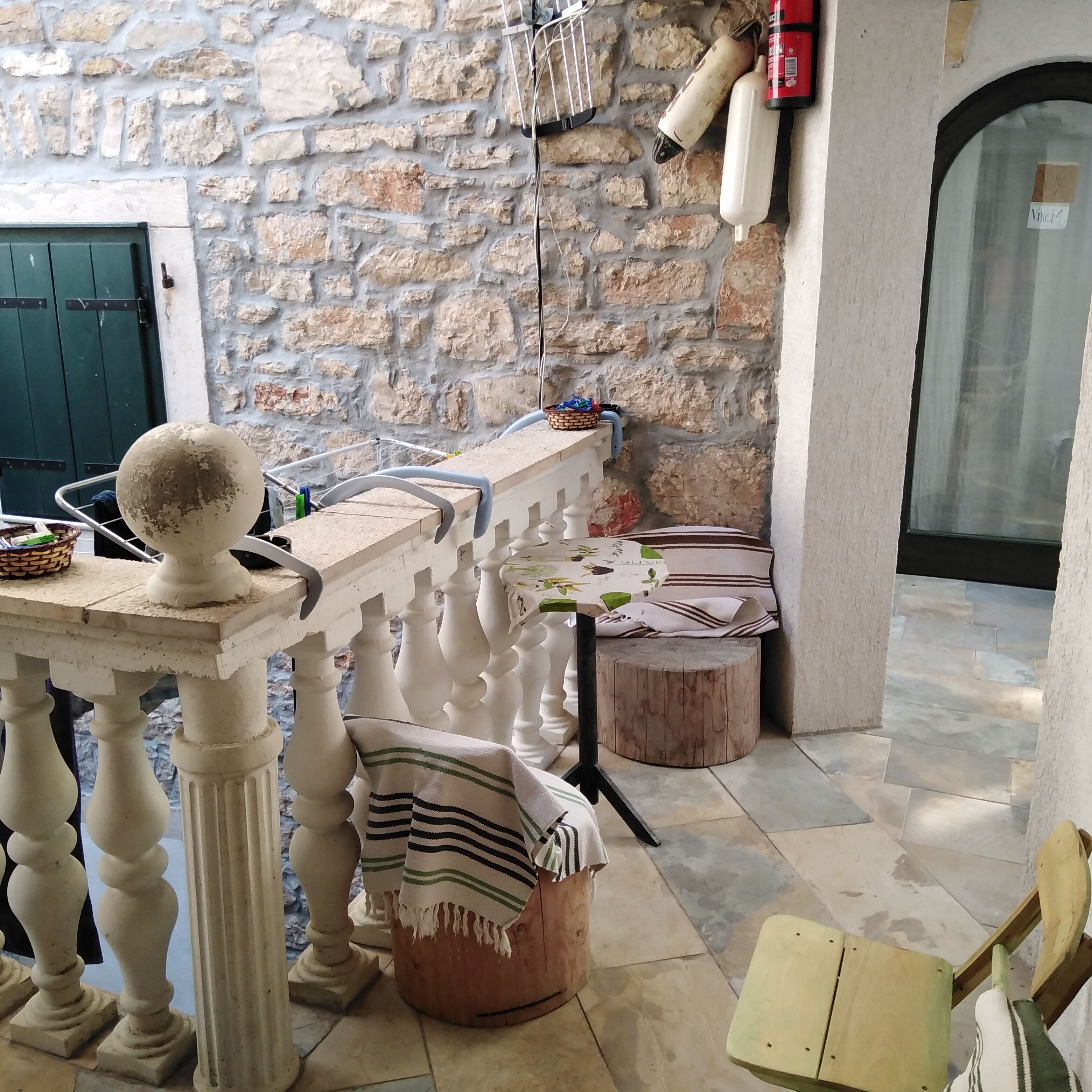 Un espacio al aire libre rústico con un muro de piedra, una mesa de madera con un objeto decorativo, un banco y un taburete pequeño.