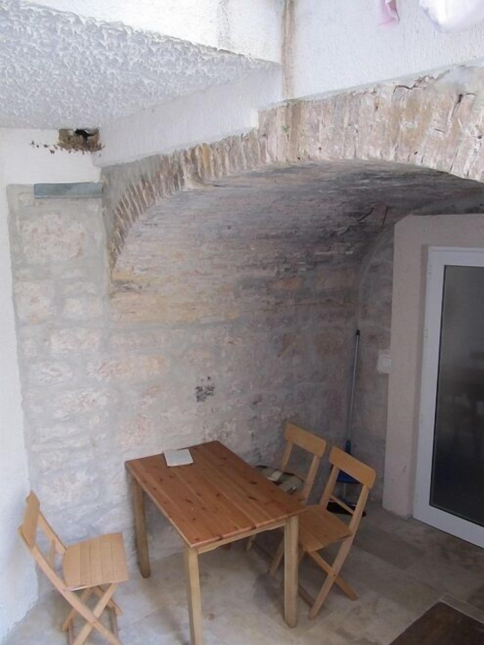 A room with a stone wall, a wooden table with chairs, and a door with a screen.