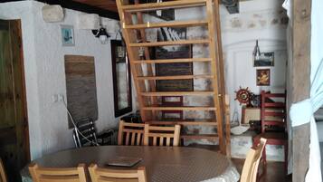 Un comedor con una mesa redonda, sillas de madera, un ventilador de techo y una estantería de escalera de madera.