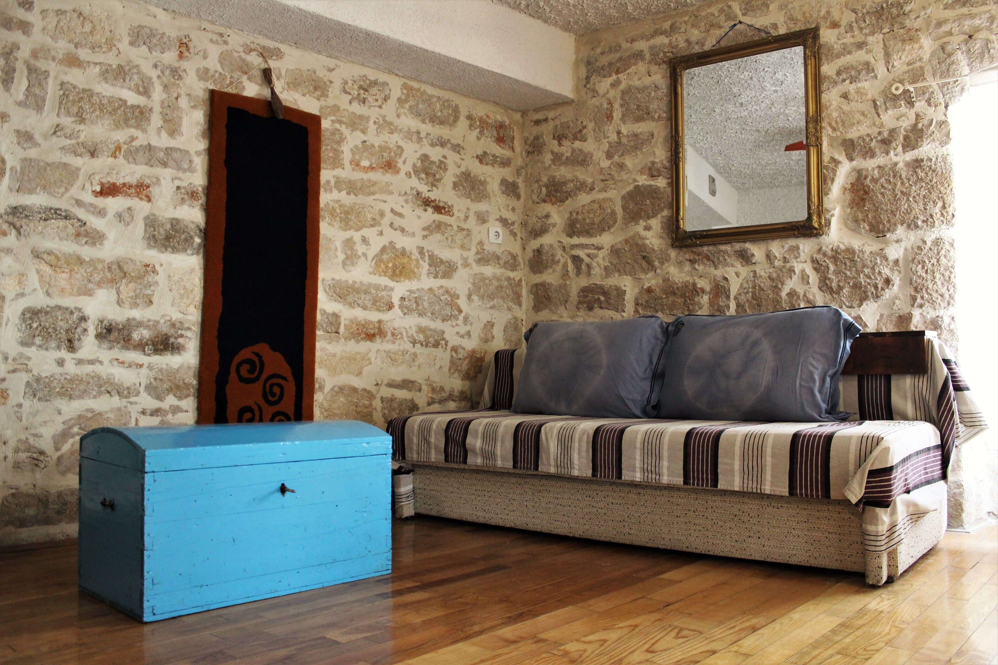 A room with a stone wall, a sofa with striped cushions, a blue chest of drawers, and a mirror on the wall.