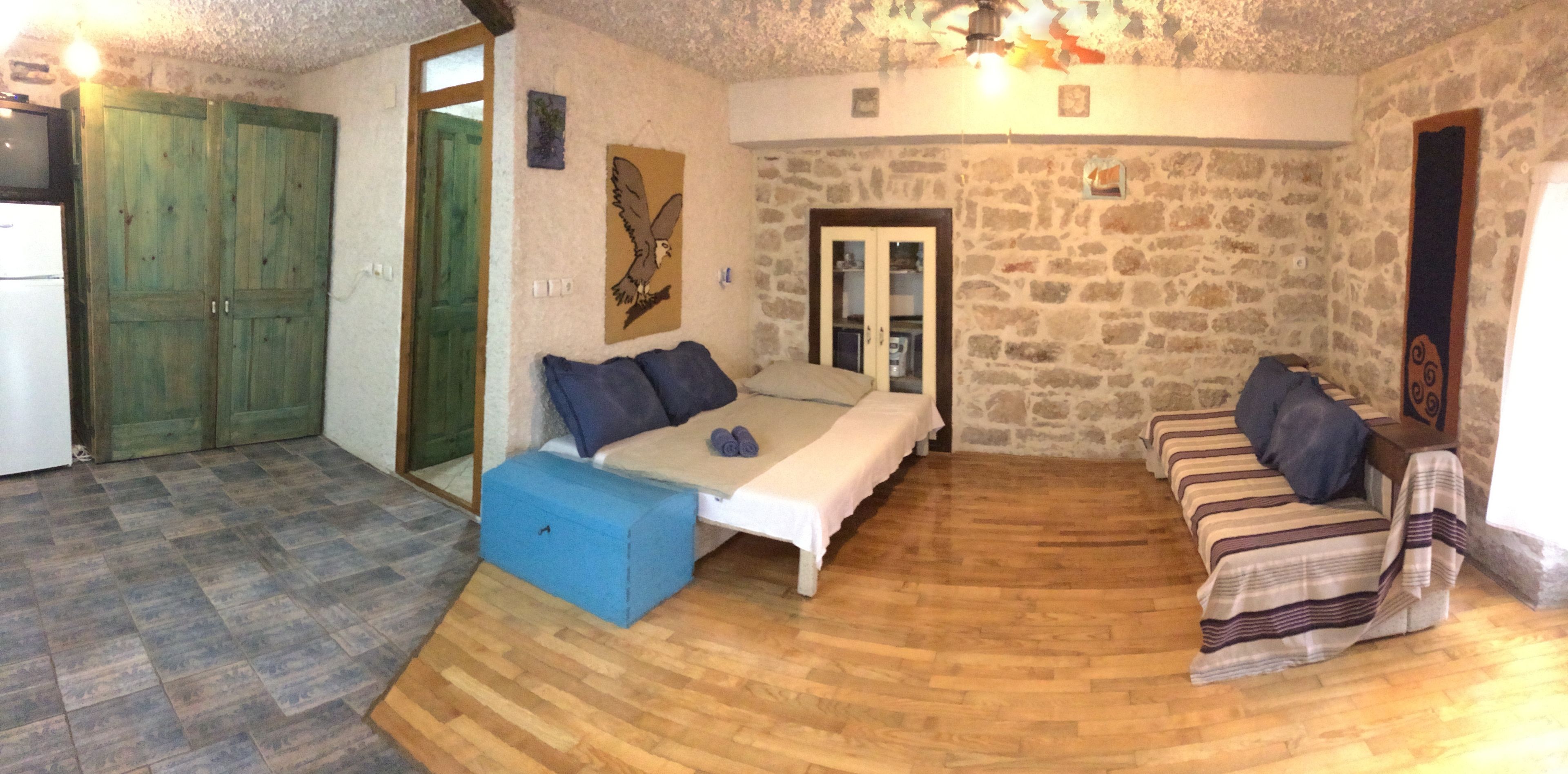A cozy room with a bed, a sofa, and a small table. There is a stone wall and a wooden floor.