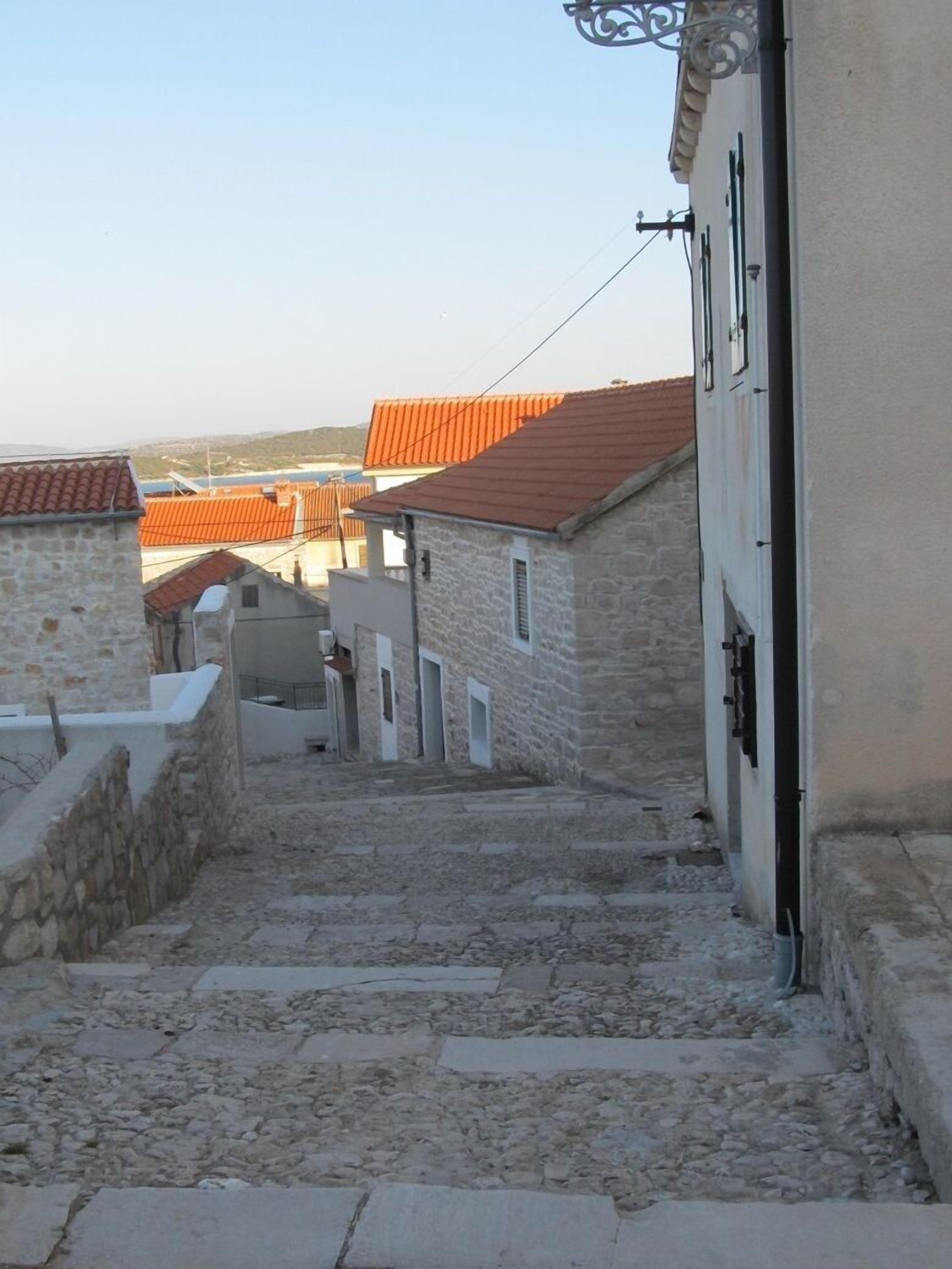 A narrow stone pathway leading to a building with a red-tiled roof.
