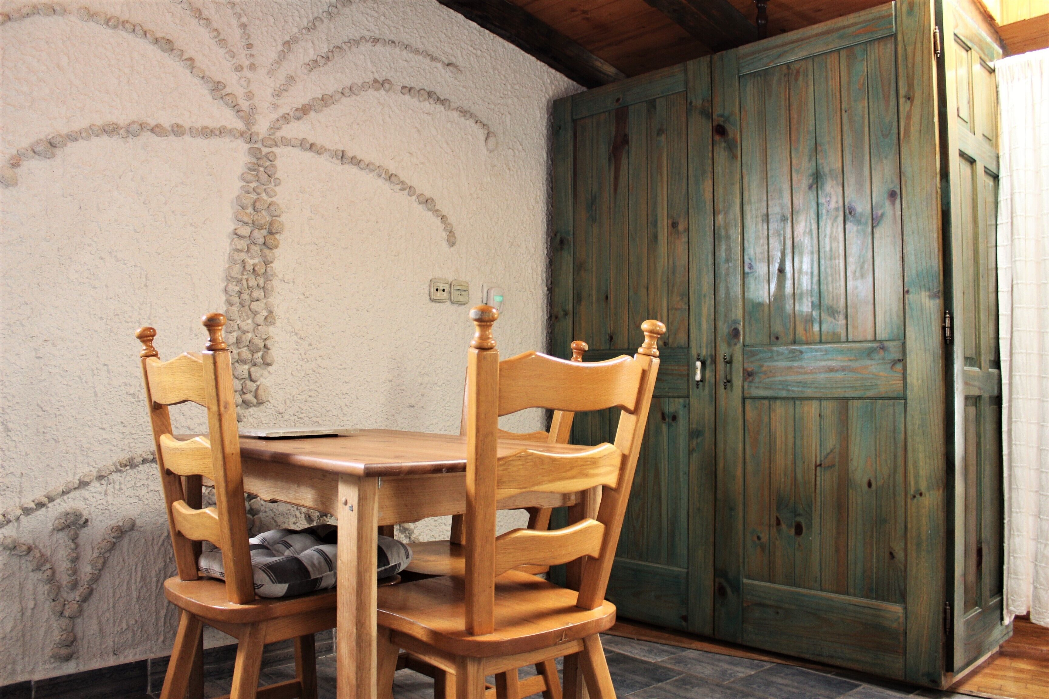 A wooden dining table with four chairs, a wall with a palm tree design, and a wooden door.