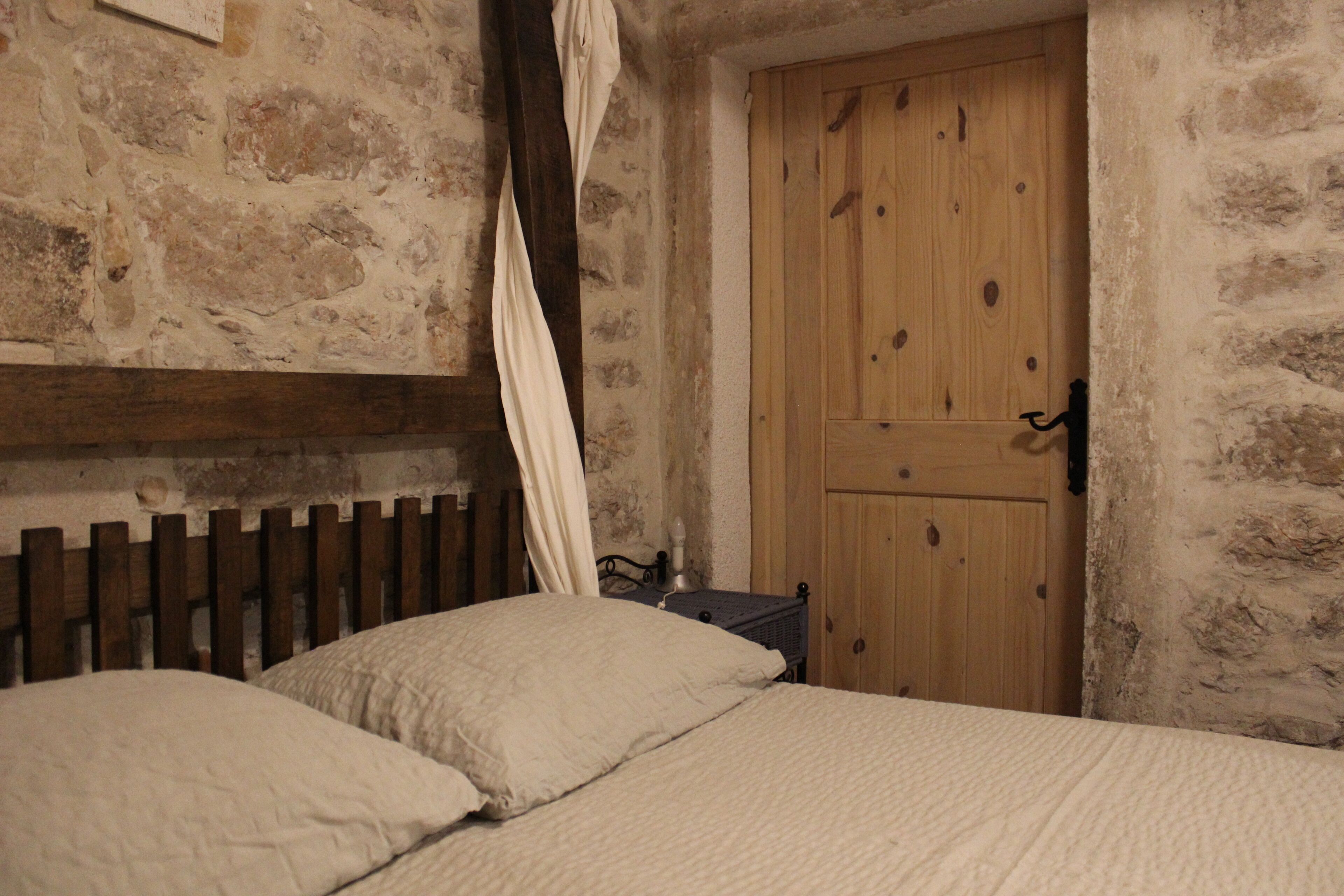 Una habitación rústica con pared de piedra, puerta de madera y cama con ropa blanca.