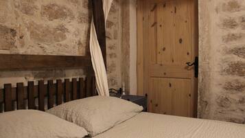 Una habitación rústica con pared de piedra, puerta de madera y cama con ropa blanca.