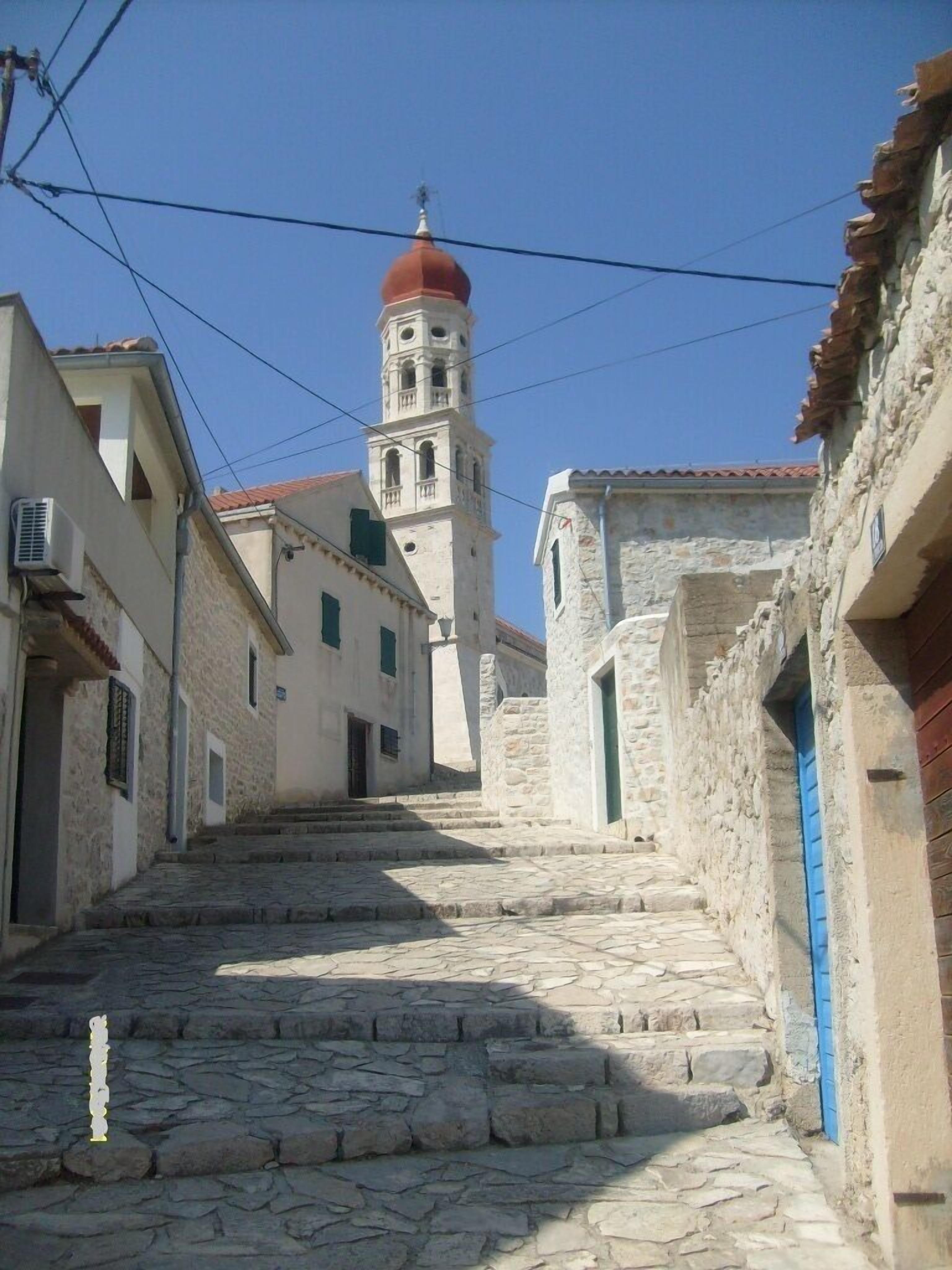 A narrow stone-paved street leading to a church with a red dome and bell tower.