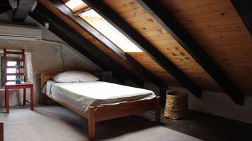 Una cama individual en una habitación con techo inclinado y tragaluz, una silla y un recipiente de piedra.