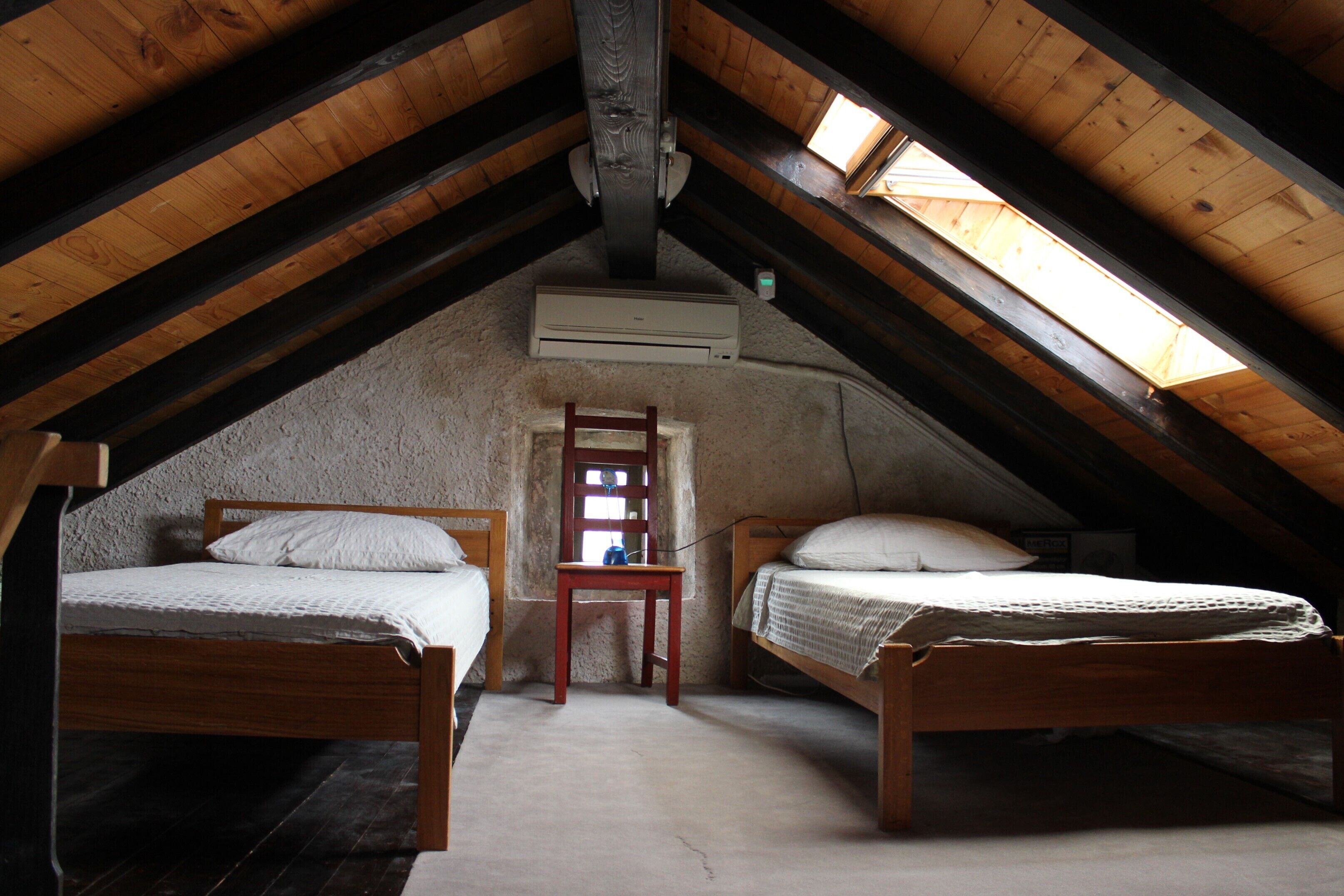 Une petite chambre mansardée avec deux lits en bois, une chaise en bois et une fenêtre.