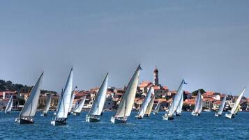Eine Küstenstadt mit Segelbooten auf dem Wasser, Häusern mit roten Dächern und einem Turm im Hintergrund.