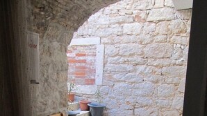 A stone-walled courtyard with a wooden ladder leaning against a wall, a set of stone steps, and potted plants. - Murter Voltera (Tisno)