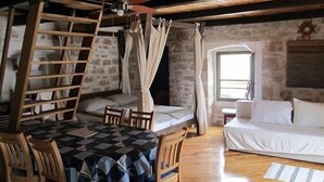 A rustic room with a wooden table and chairs, a bed with white linens, a wooden ladder, and a ceiling fan. - Murter Voltera (Tisno)