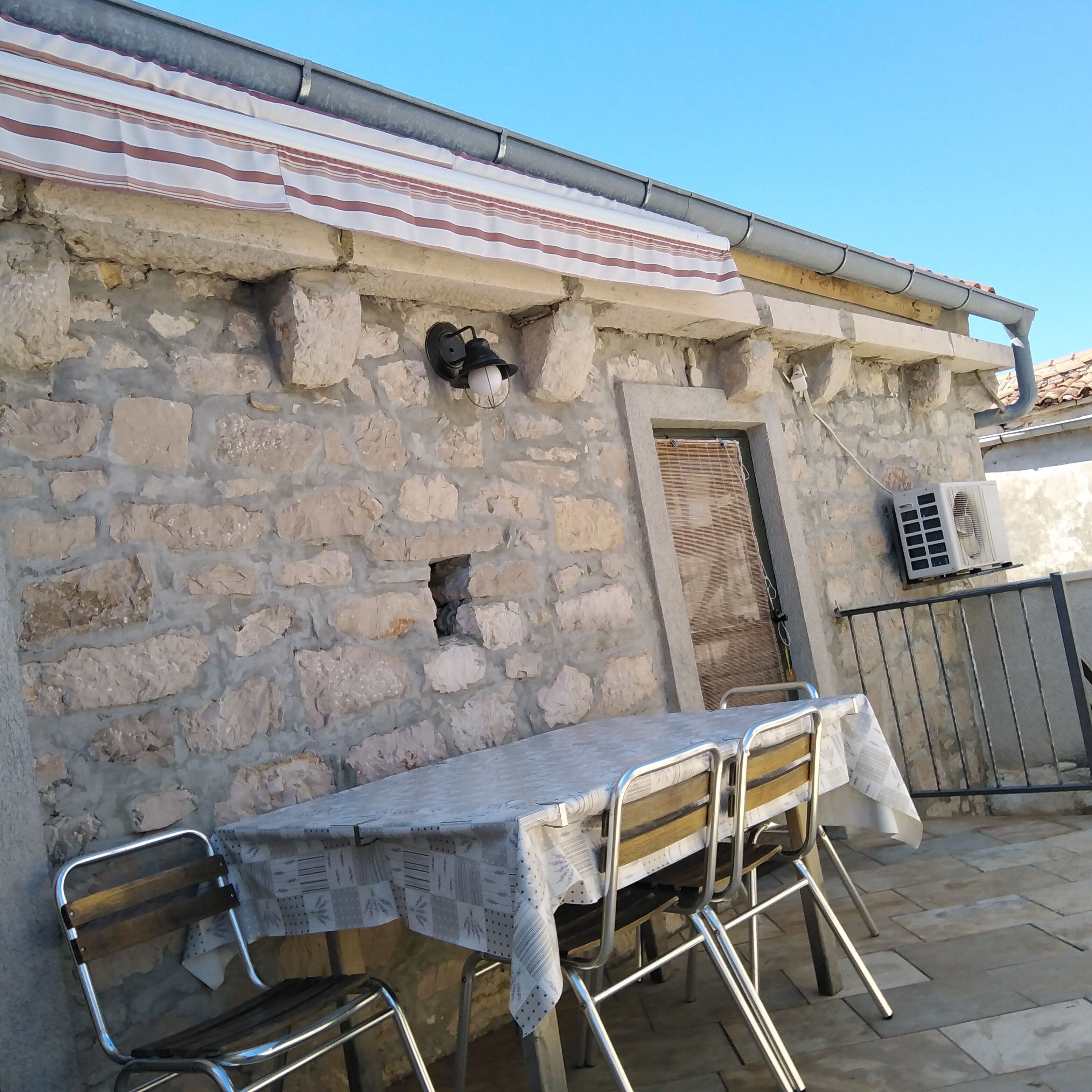 Un muro de piedra con una puerta, un ventanal pequeño y una mesa con sillas.