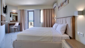 A hotel room with a large bed, a desk, a chair, and a view of the sea. - Harmony Rethymno Beach Hotel (Rethymno)