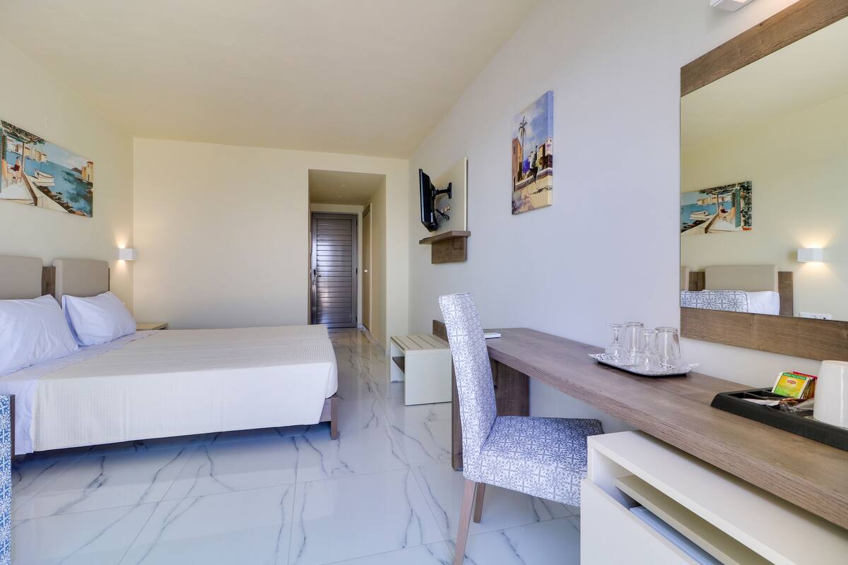 A hotel room with a bed, a desk, a chair, a TV, and artwork on the walls.