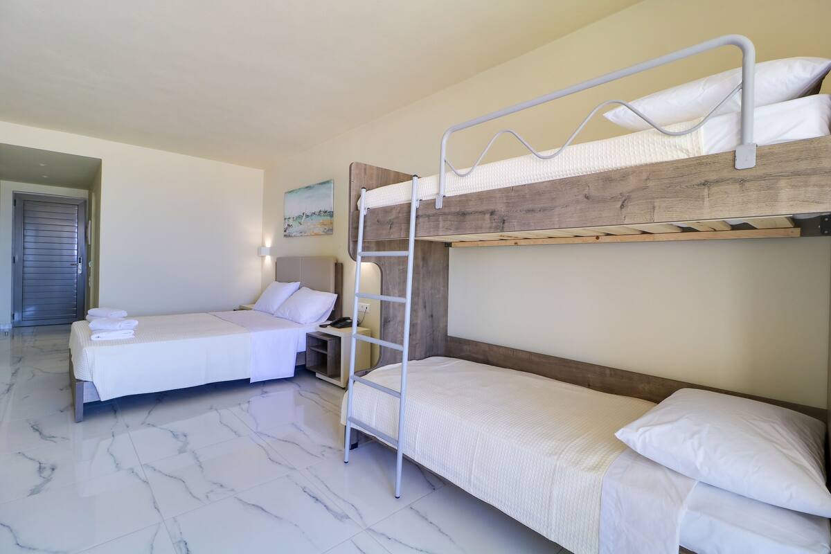 A hotel room with two beds, one with a wooden headboard and the other with a metal frame. A ladder is placed between the beds.