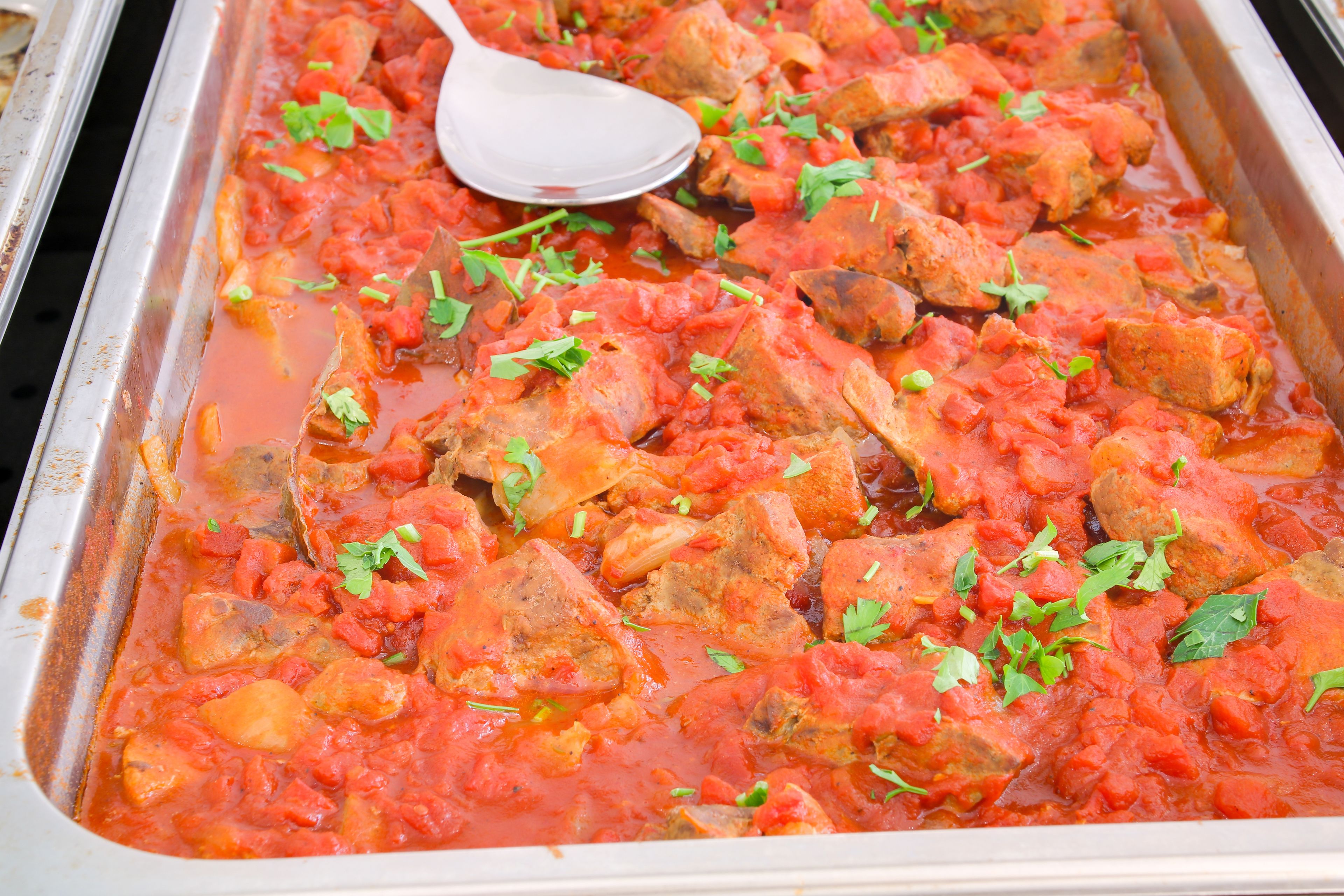 Un plato de estofado con trozos de carne y verduras en salsa de tomate, adornado con hierbas.