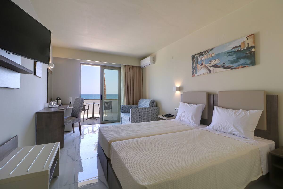 A hotel room with two beds, a desk, a chair, a TV, and a painting on the wall.