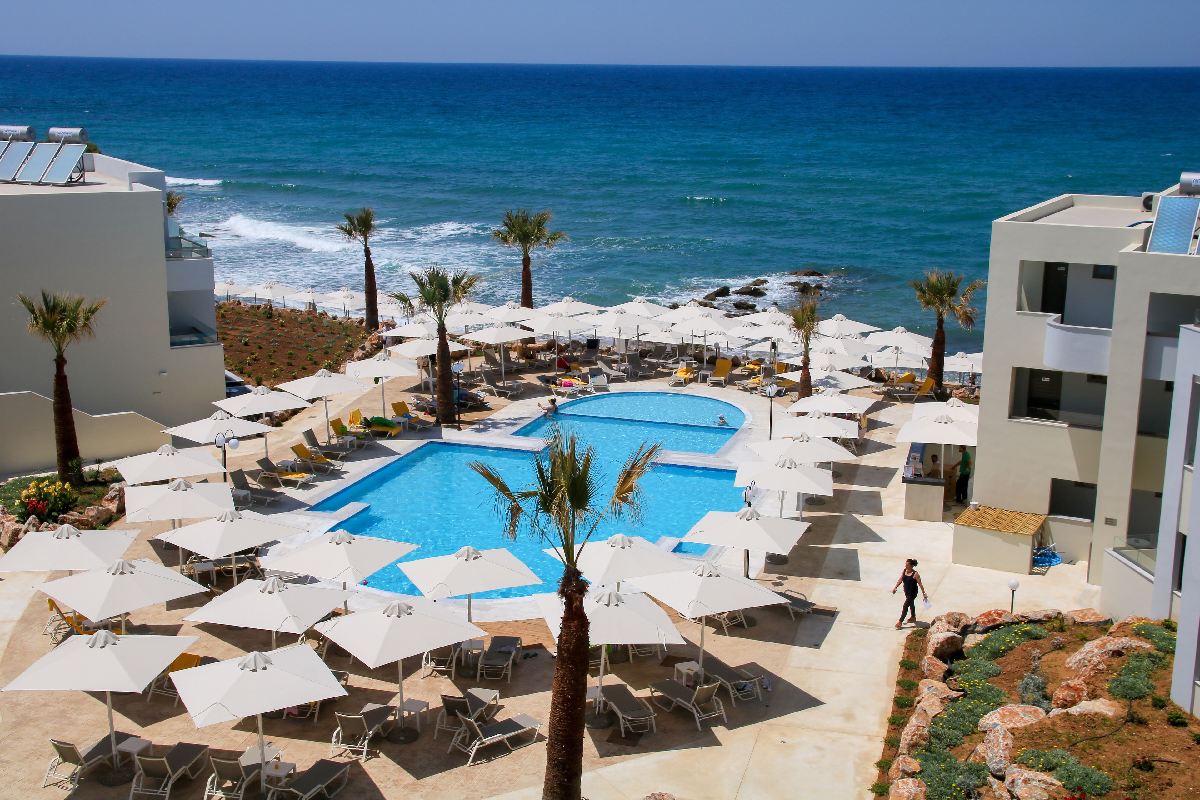 A resort pool area with multiple pools, sun loungers, umbrellas, and a view of the ocean.