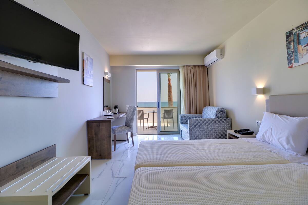 A hotel room with a large bed, a desk, a chair, a TV, and a balcony with a view.