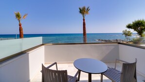 A balcony with a table and chairs, overlooking a beach with palm trees and the sea. - Harmony Rethymno Beach Hotel (Rethymno)