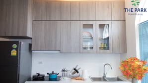 A modern kitchen with wooden cabinets, a built-in oven, a sink, and a window with blinds. - The Park Vientiane (Vientiane)