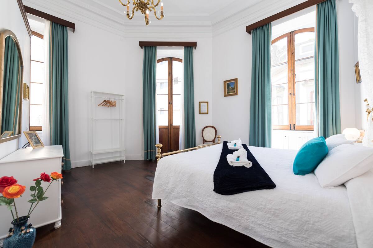 A hotel room with a large bed, a dresser, a vanity, and a window with curtains.