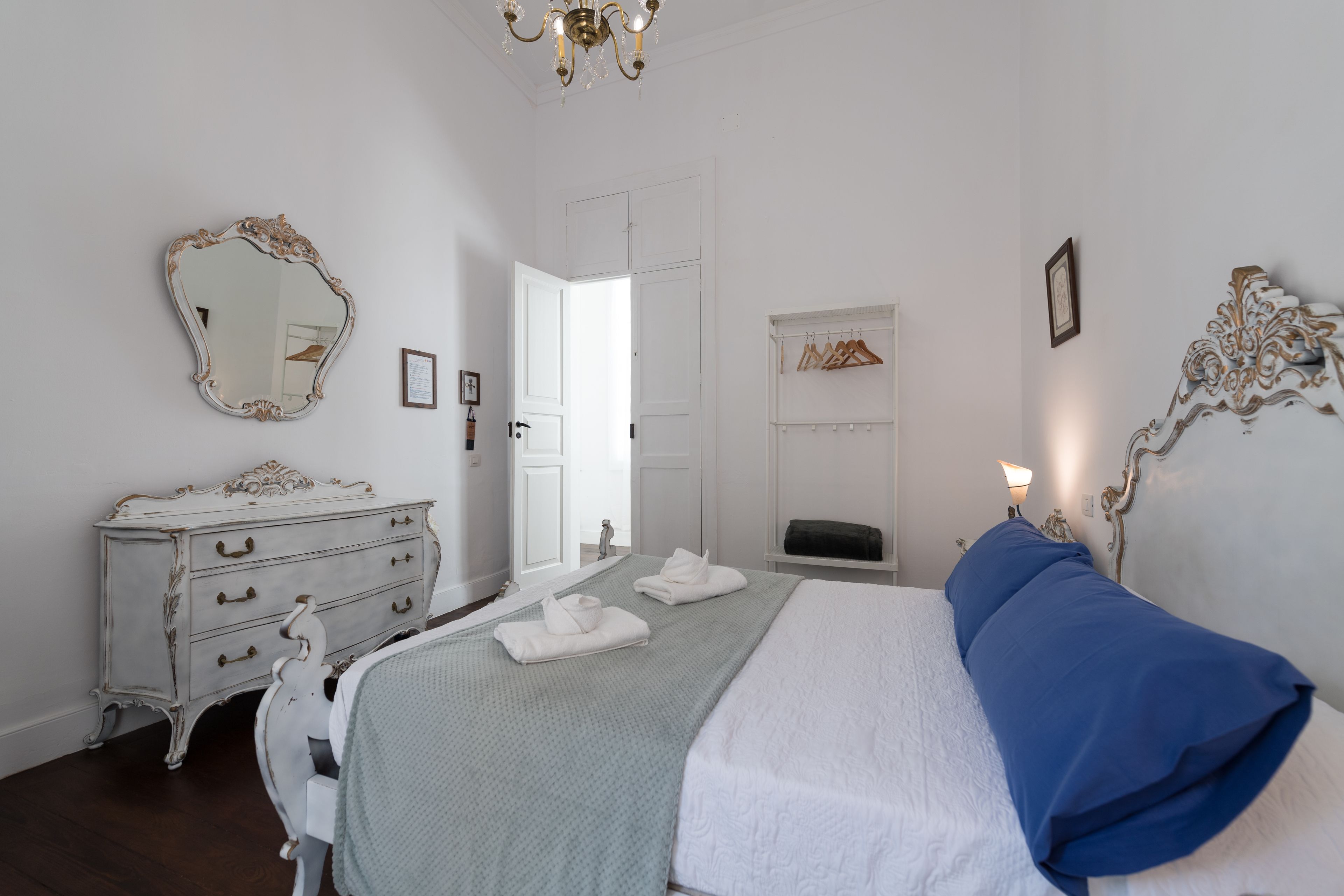 A bedroom with a bed, dresser, mirror, and a door leading to another room.