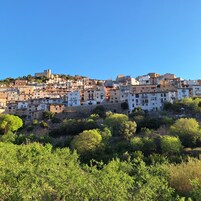 Un pueblo situado en una ladera con muchas construcciones históricas y una imponente estructura que recuerda a un castillo en la cima.