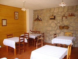 Un comedor con mesas y sillas de madera, paredes de piedra y un ambiente rústico.