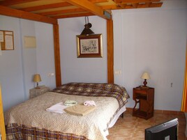Un dormitorio con cama, mesita de noche, lámpara, un cuadro en la pared y televisión.