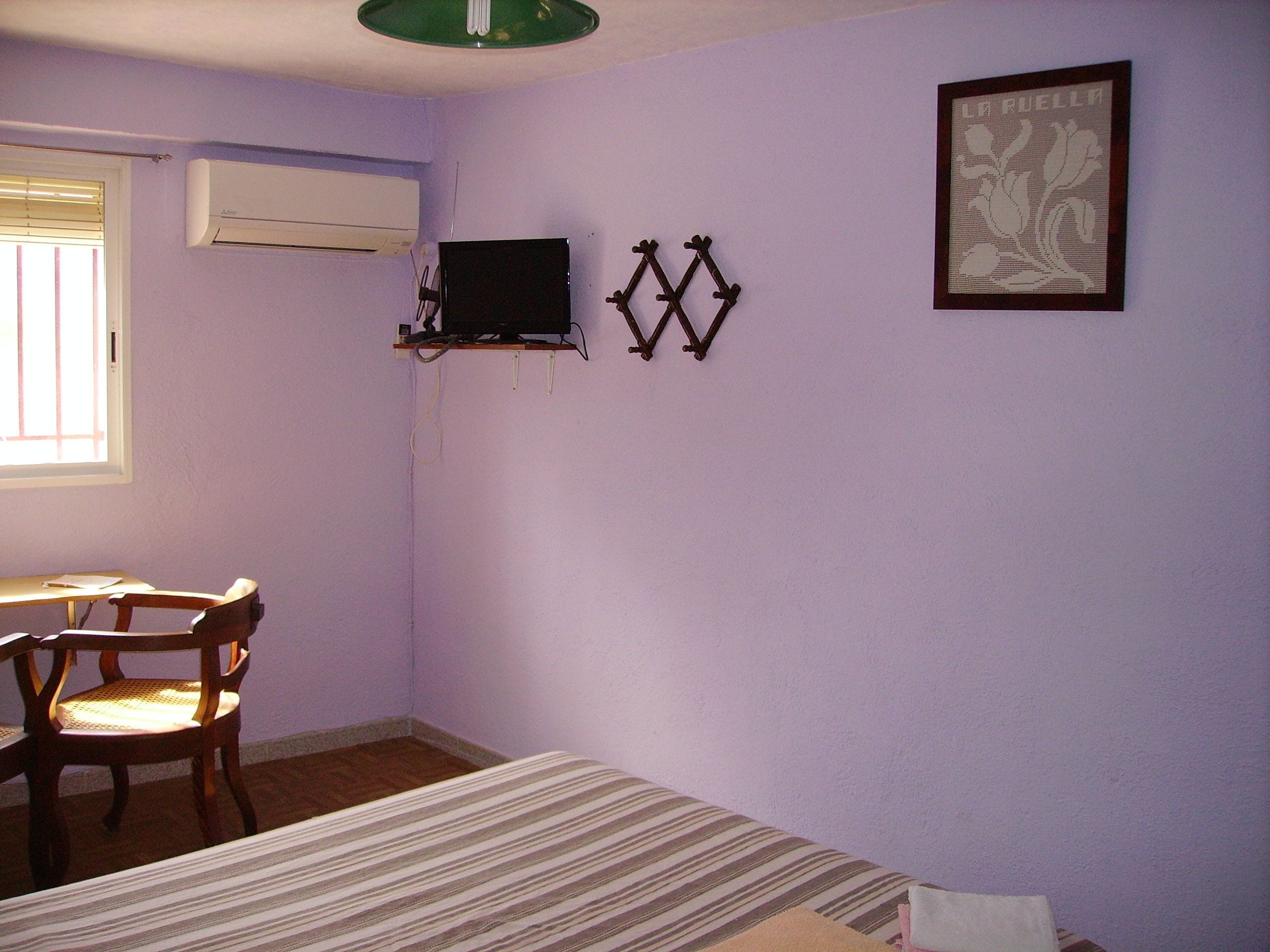 A room with a bed, a desk, a chair, an air conditioner, and a wall-mounted decoration.