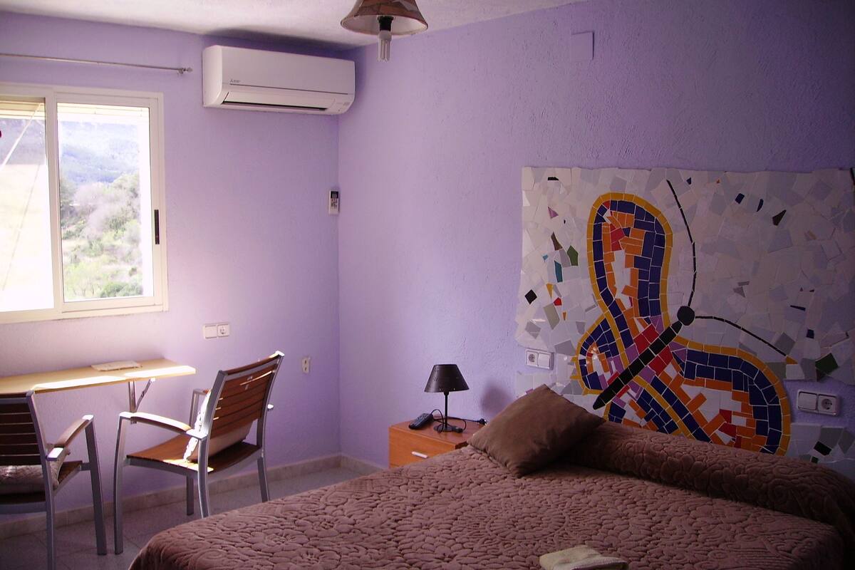 A bedroom with a bed, a desk, a chair, and a wall with a mosaic artwork.