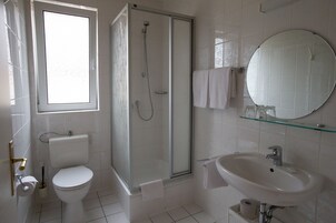 A modern bathroom with a toilet, shower, sink, and a large mirror.