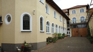 Um edifício com várias janelas em arco, uma porta de madeira e um pátio pavimentado.