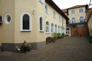 A building with multiple arched windows, a wooden door, and a paved courtyard.