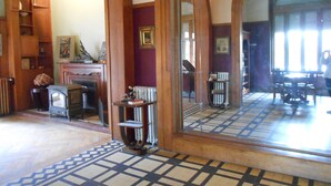 A room with a large mirror reflecting the interior, wooden arches, a patterned floor, and a fireplace with a mantel. - La Passagère (Hauterive)