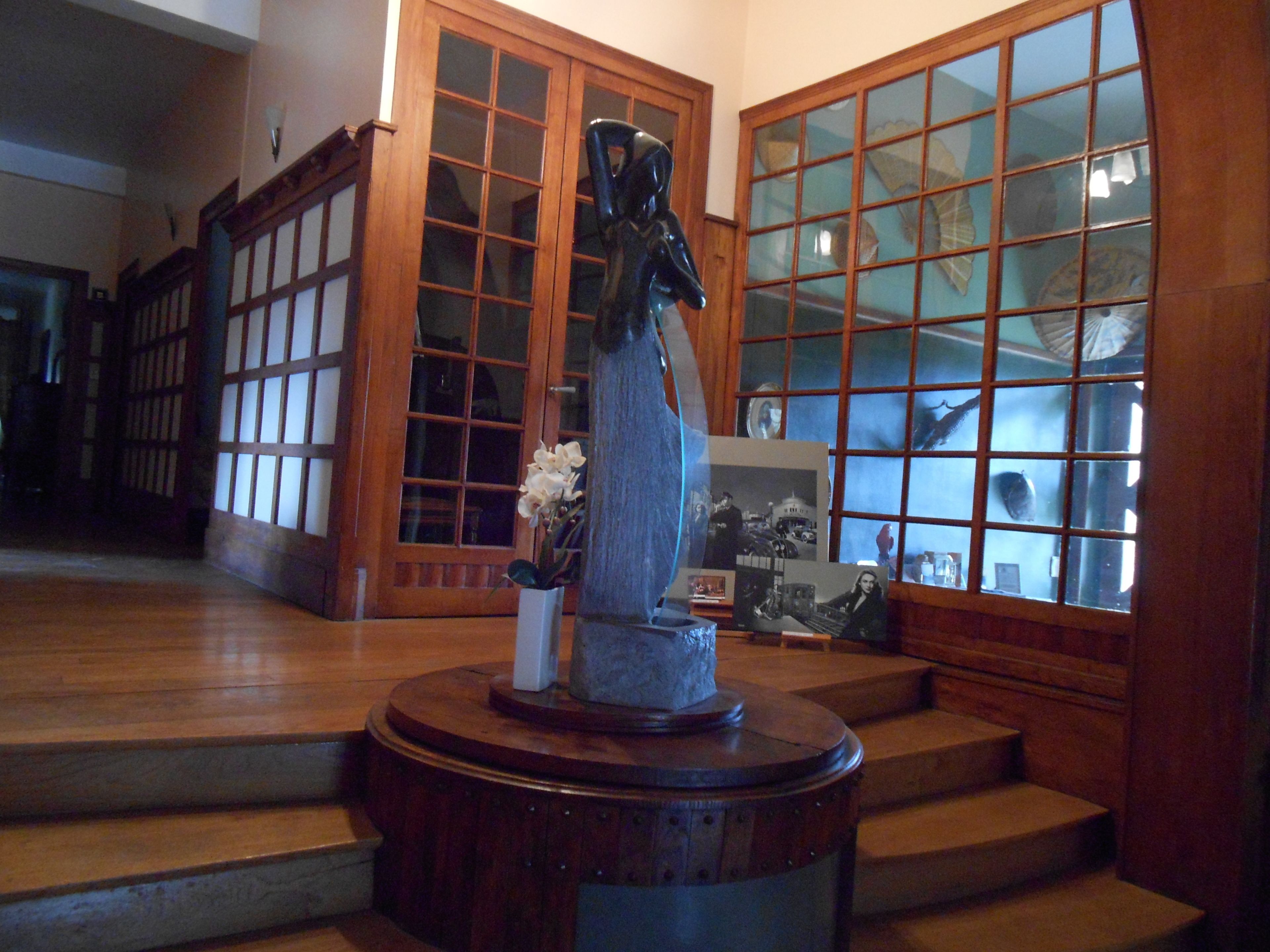 A statue on a pedestal in a room with wooden flooring and large glass doors.