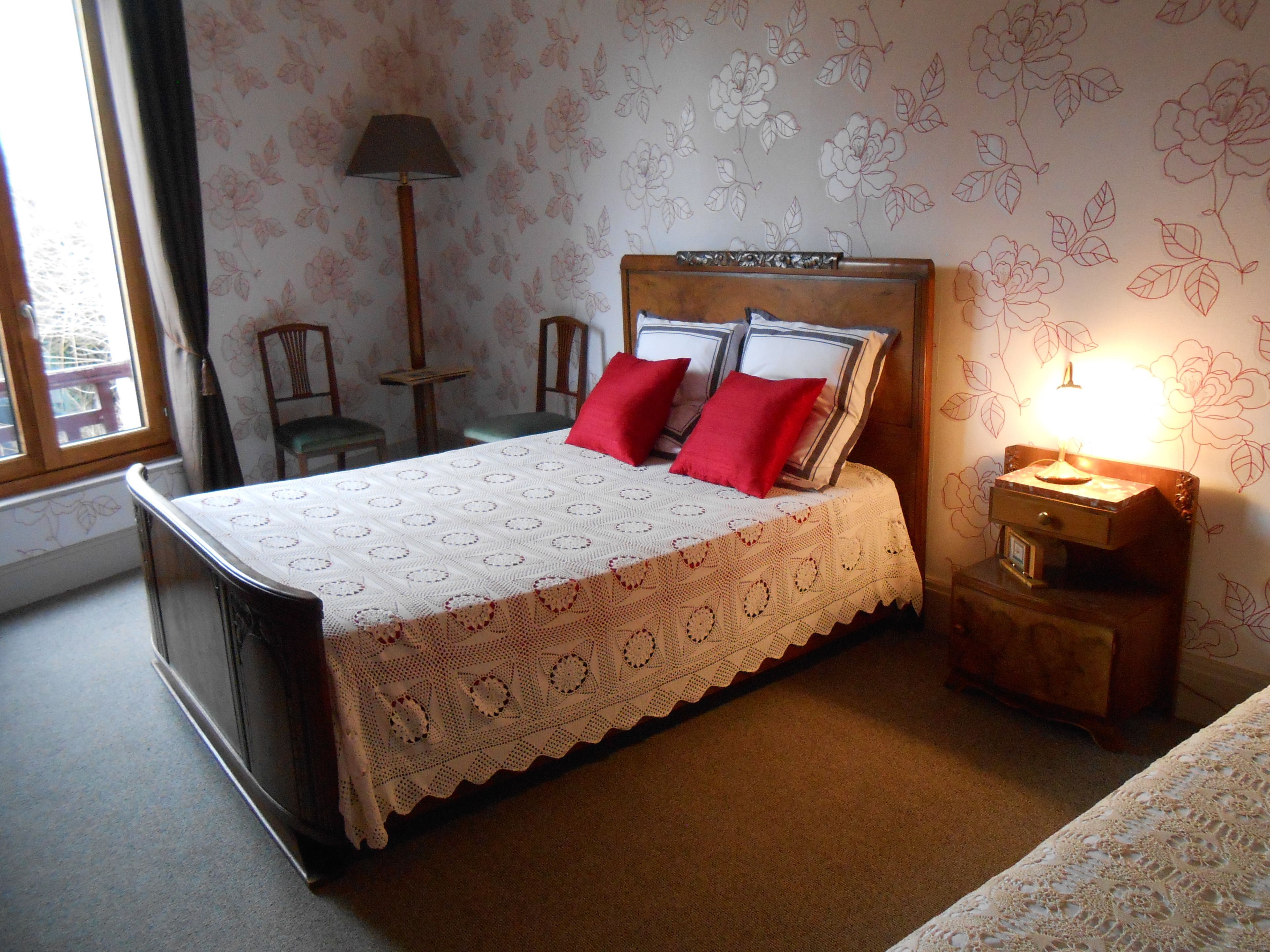 A neatly made bed with a white and red patterned bedspread, a wooden headboard, and a bedside table with a lamp.