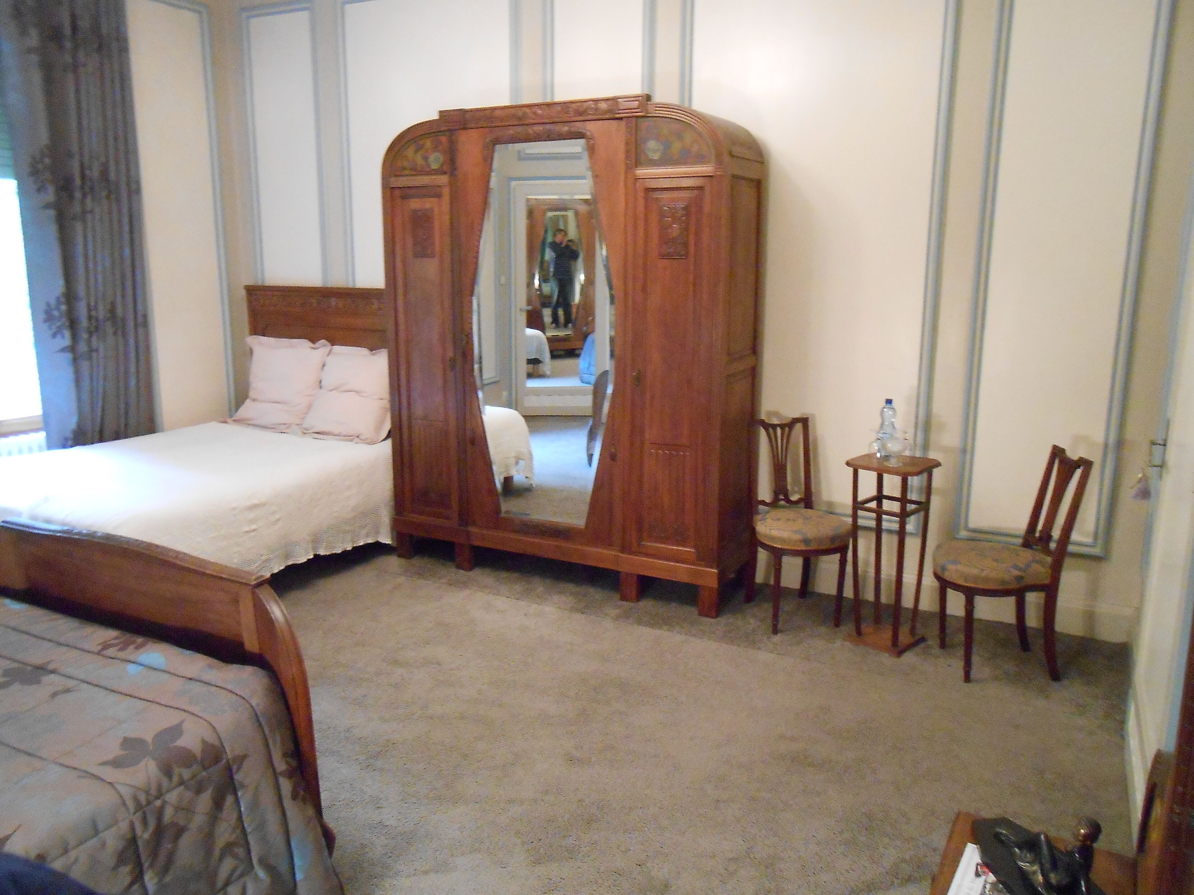 A bedroom with a bed, a wooden wardrobe with a mirror, two chairs, and a small table.