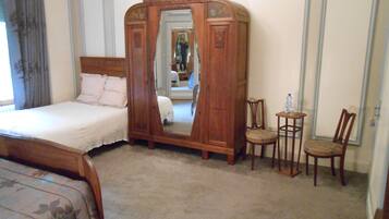 A bedroom with a bed, a wooden wardrobe with a mirror, two chairs, and a small table.
