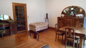 Un comedor con una mesa y sillas de madera, un sofá, un aparador de madera y un espejo.