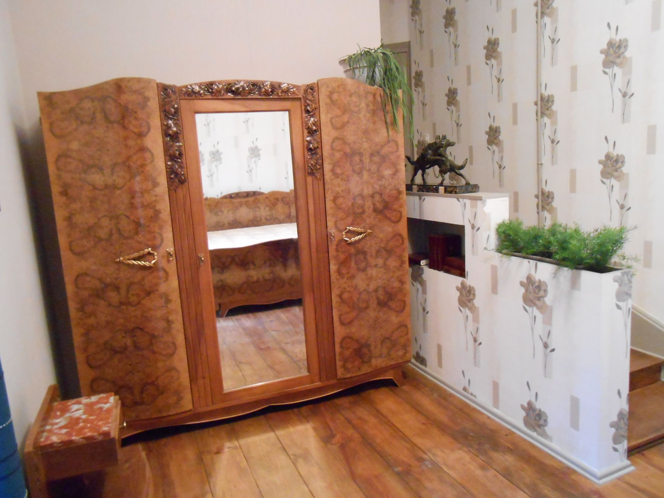 A room with a wooden wardrobe, a small table with a plant, and floral wallpaper.