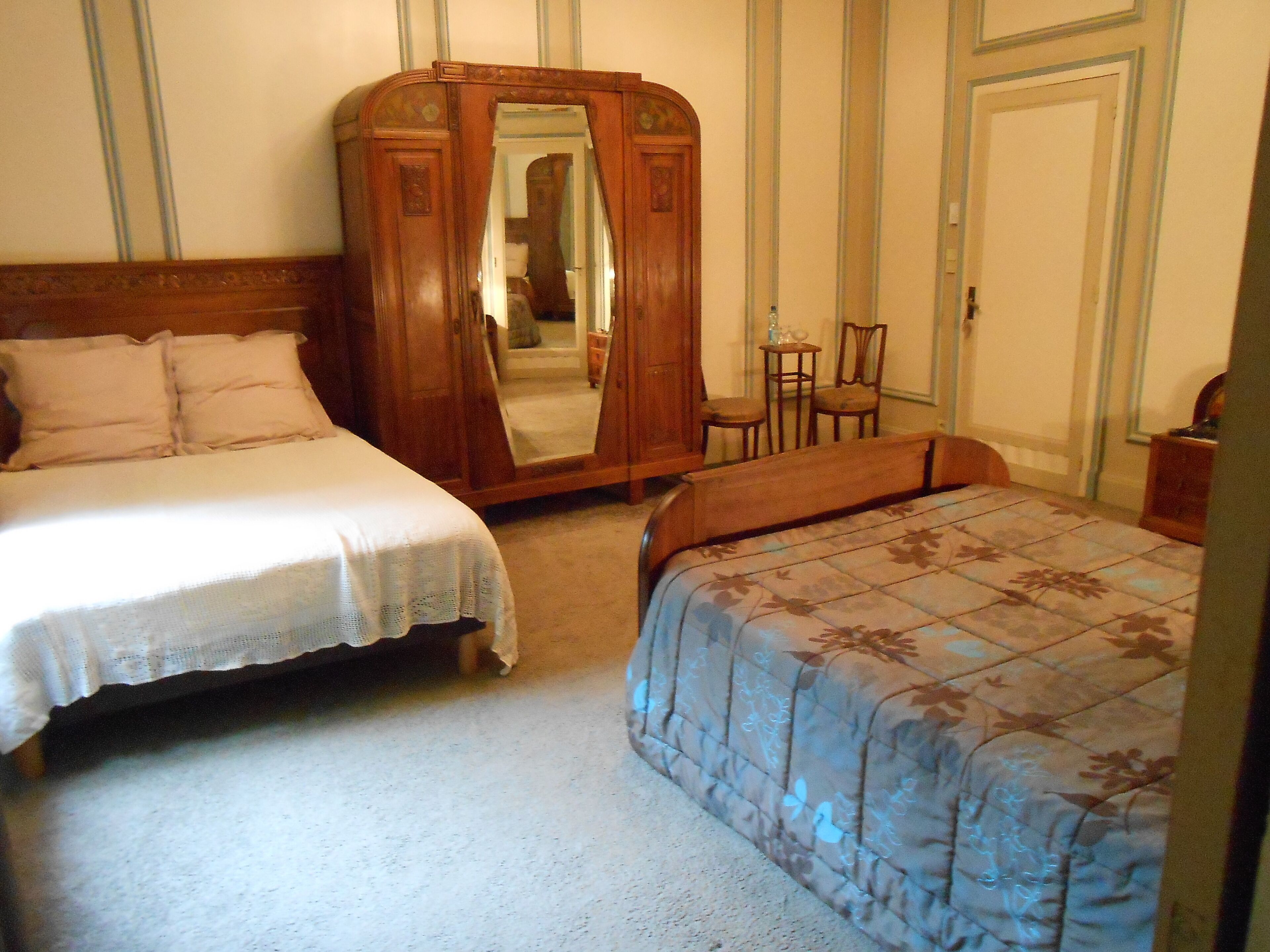 Une chambre avec deux lits, une armoire en bois et un miroir.