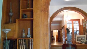 A room with wooden shelving filled with books and decorative items, a patterned floor, and an arched doorway leading to another room. - La Passagère (Hauterive)