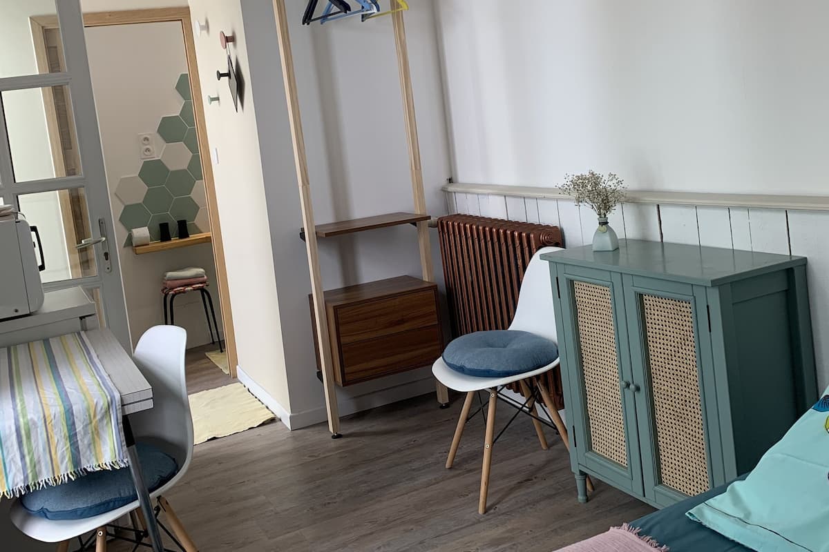 A room with a bed, a desk, a chair, a radiator, and a hanging light fixture.