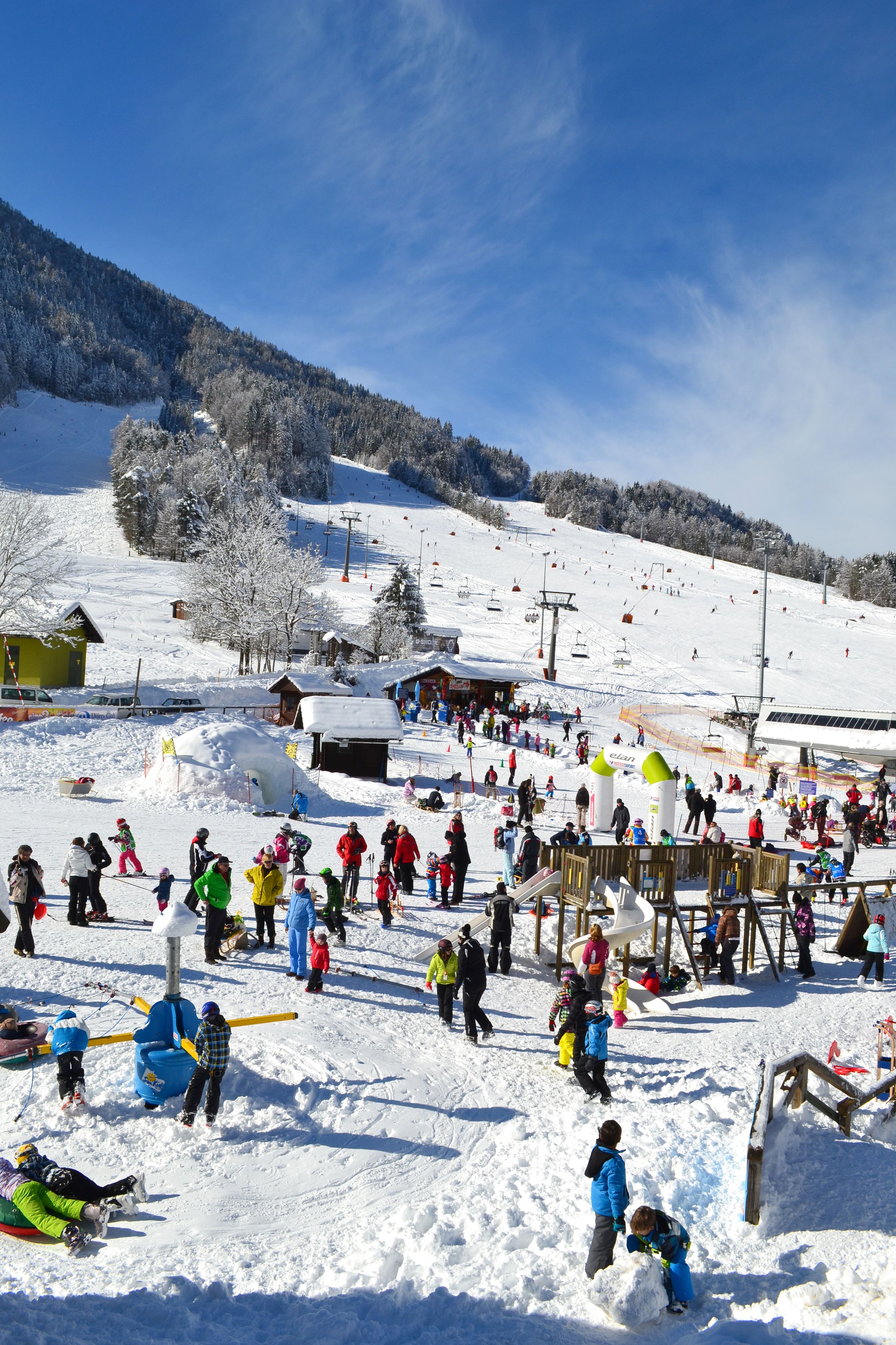 A snowy ski resort with a ski lift, snow-covered trees, and a clear blue sky.