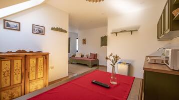 A room with a red carpet, a wooden cabinet with floral carvings, a remote control, and a vase with flowers on a table.