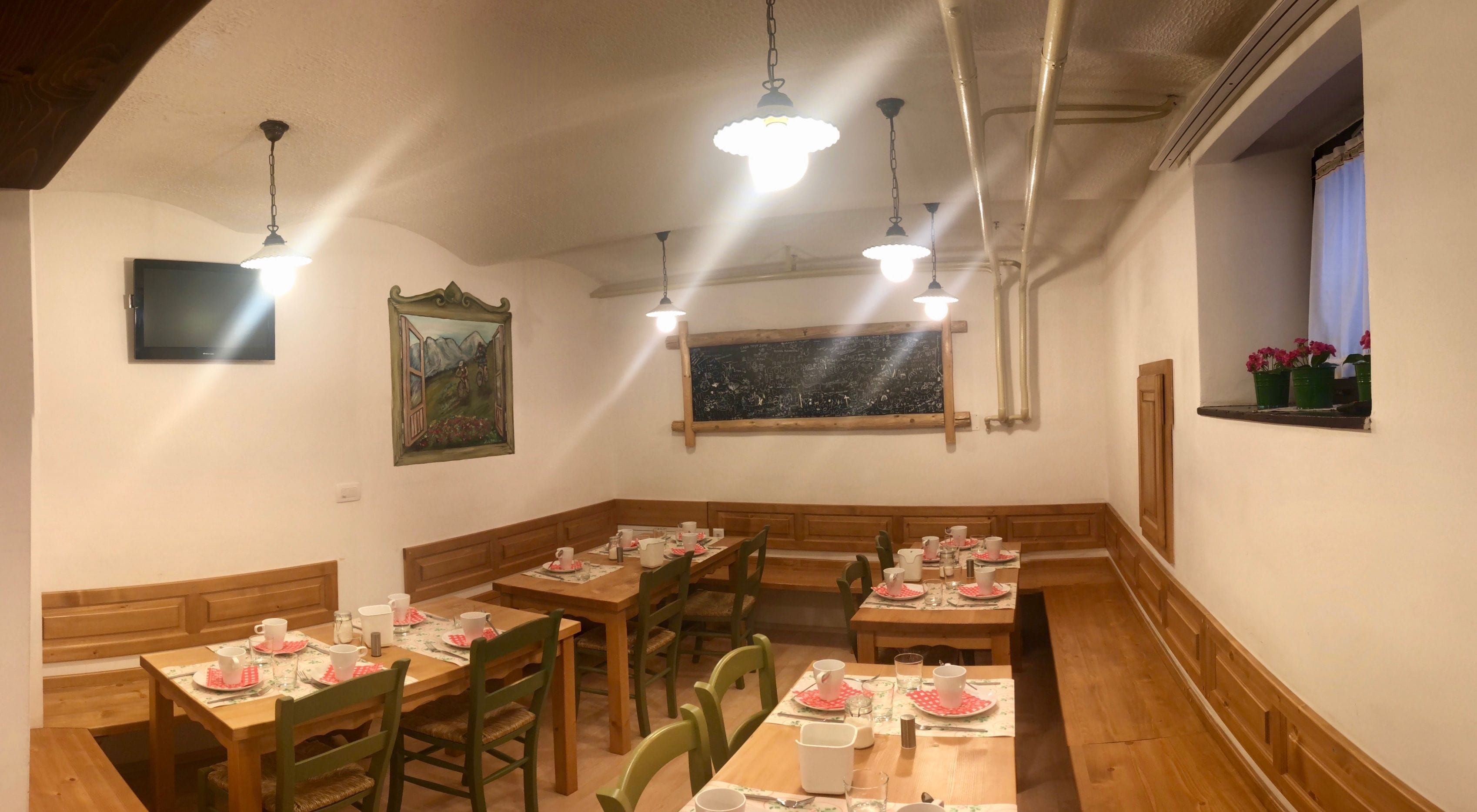 A dining area with wooden tables and chairs, a blackboard with chalk drawings, and a window with flowers.